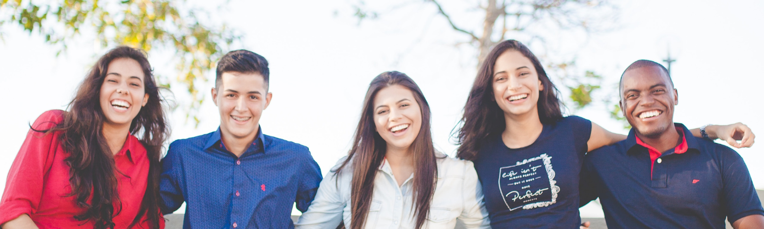 Image of five young people sitting outside on a bench with their arms around each other.