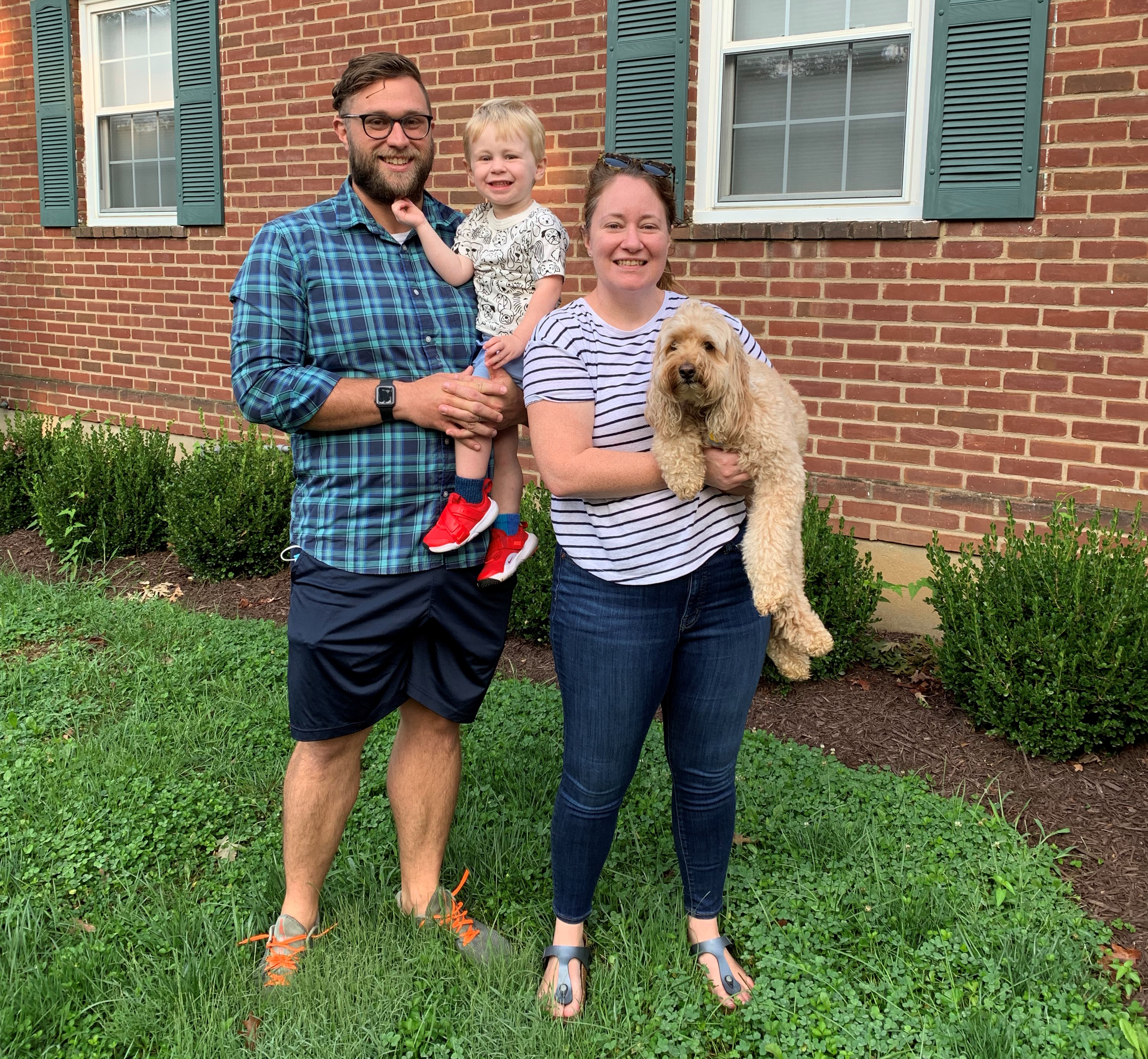 Family and dog stand together outside of brick house.